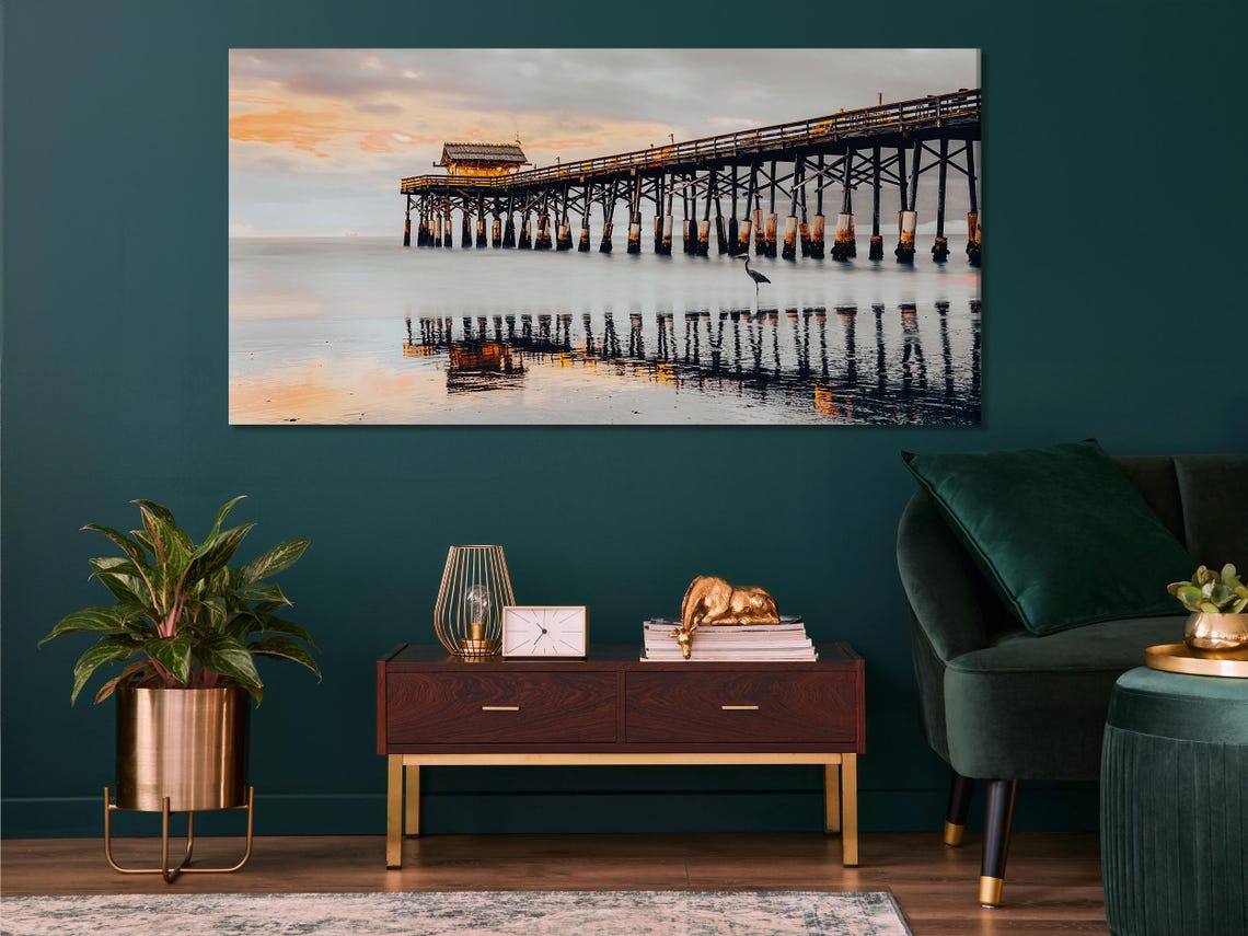 Coastal pier over calm water at sunset with reflections and a small bird on the posts detail view