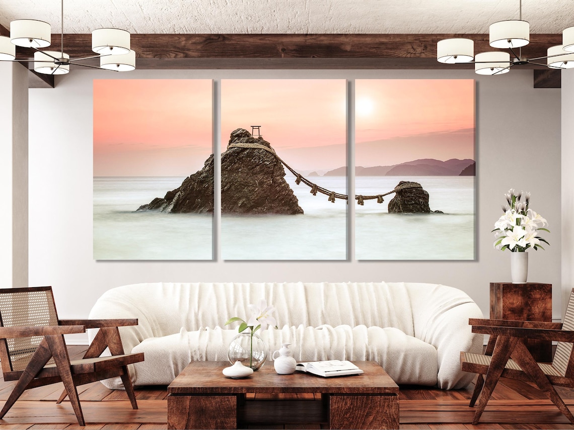 A sunset seascape shows two rocky islands connected by a rope with small posts, set against soft pink-orange skies and pale misty water detail view