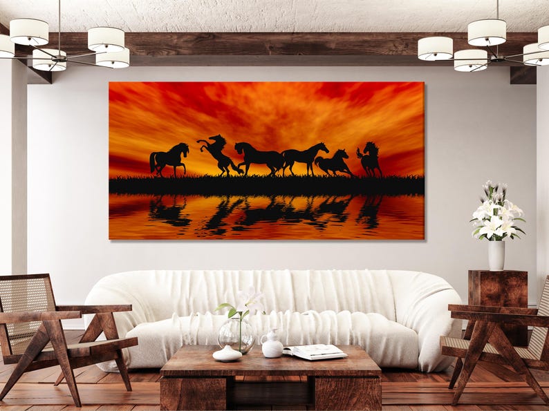 Group of horses silhouetted against a bright orange-red sunset with mirrored water reflections