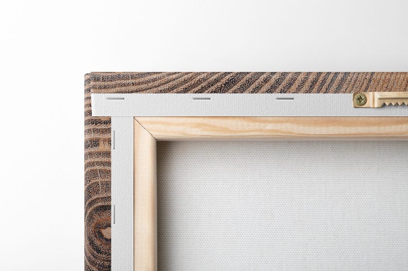 The back of a rectangular canvas print featuring a dark brown wood-grain frame. The white canvas is stretched over a light-colored wooden stretcher bar frame, secured with metal staples along the edge and a gold-toned sawtooth hanger.