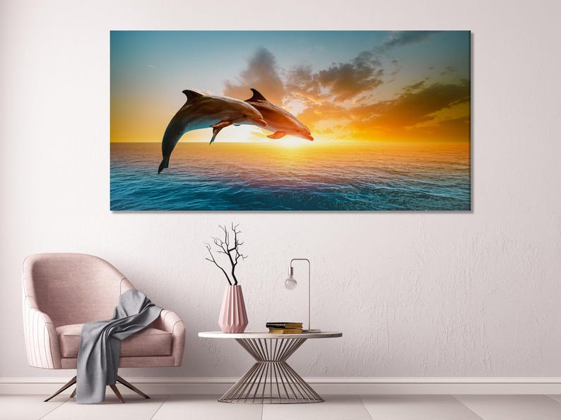 Two dolphins leaping over teal ocean waves under a golden sunset sky