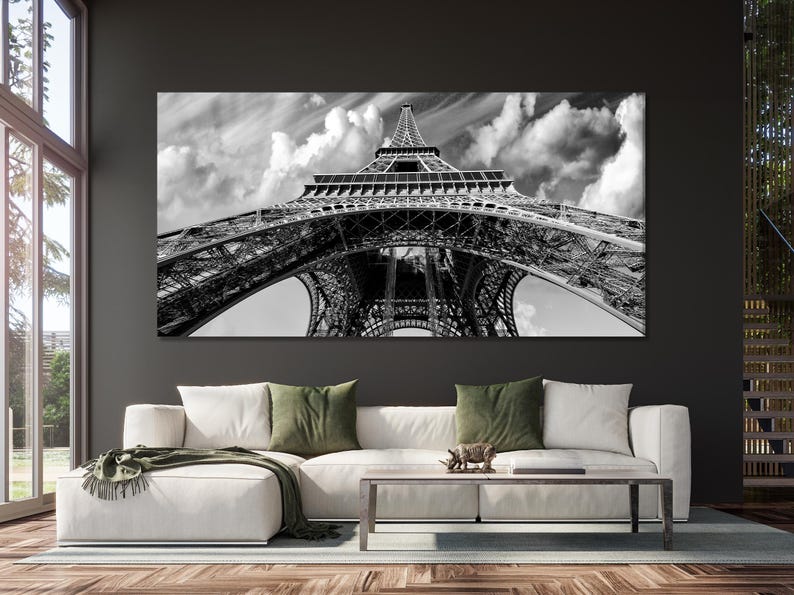 Black-and-white image of the Eiffel Tower with iron arches and a cloudy sky background
