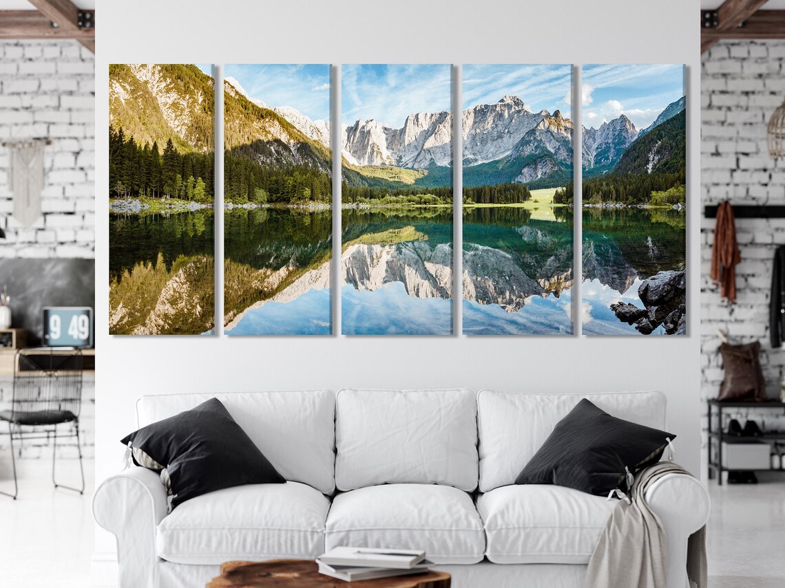 A panoramic mountain-and-lake landscape with conifer forests and clear water reflections, framed by bright sky blues and pale rocky peaks detail view