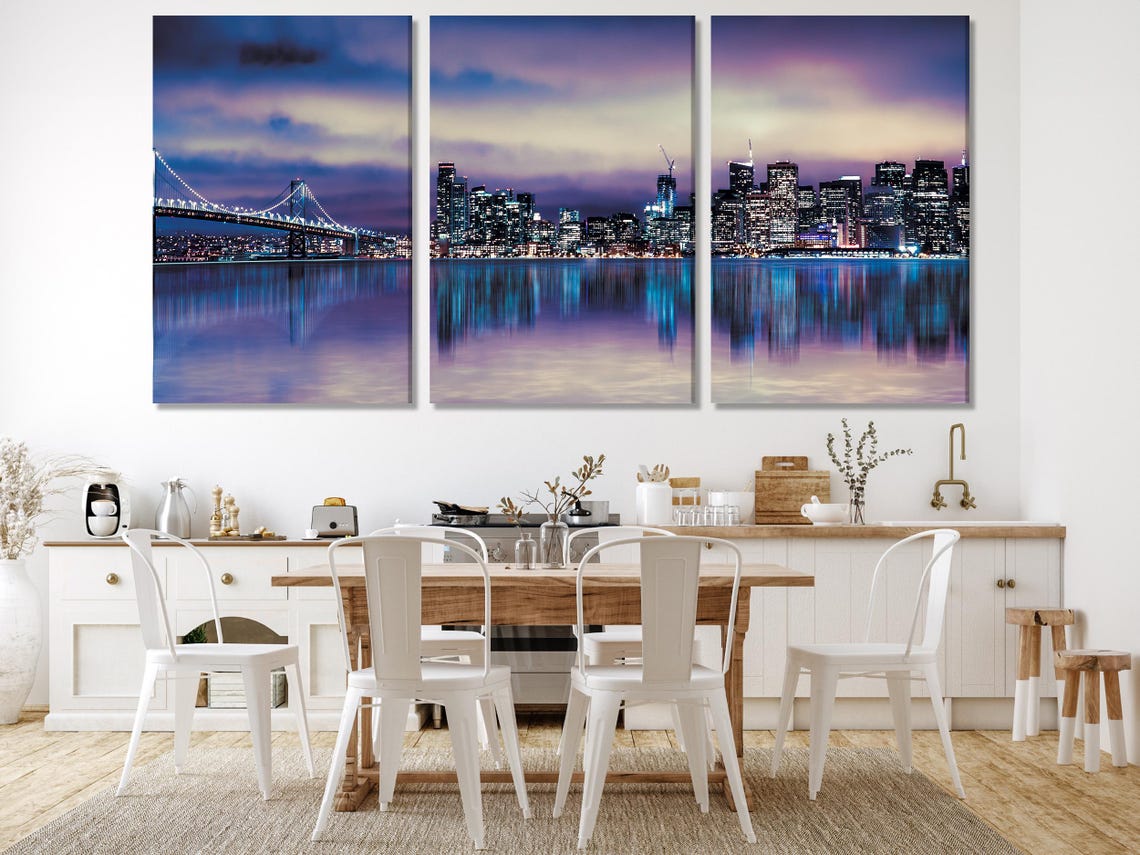 A night cityscape skyline glows in purples and blues, with a lit bridge, calm reflective water and a clouded sky detail view