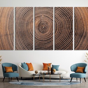 A five-panel wall art set featuring a continuous, high-resolution print of a tree trunk cross-section. The image displays concentric growth rings in shades of brown, tan, and dark charcoal, creating a detailed wood grain texture.