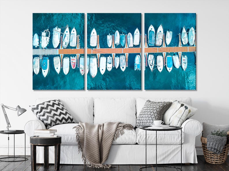 Aerial view of rows of white yachts docked along a pier in deep teal water