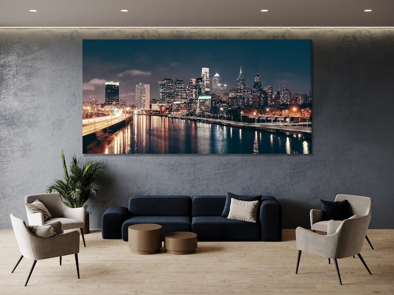 A night city skyline stretches across a wide river, with glowing building lights and shimmering reflections under a deep blue sky