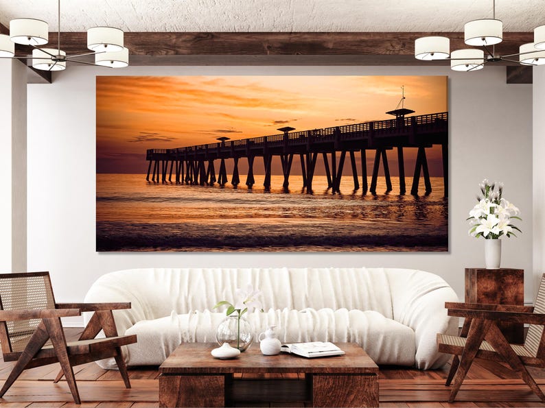 Silhouetted pier over calm ocean water at sunset with orange and gold sky colours