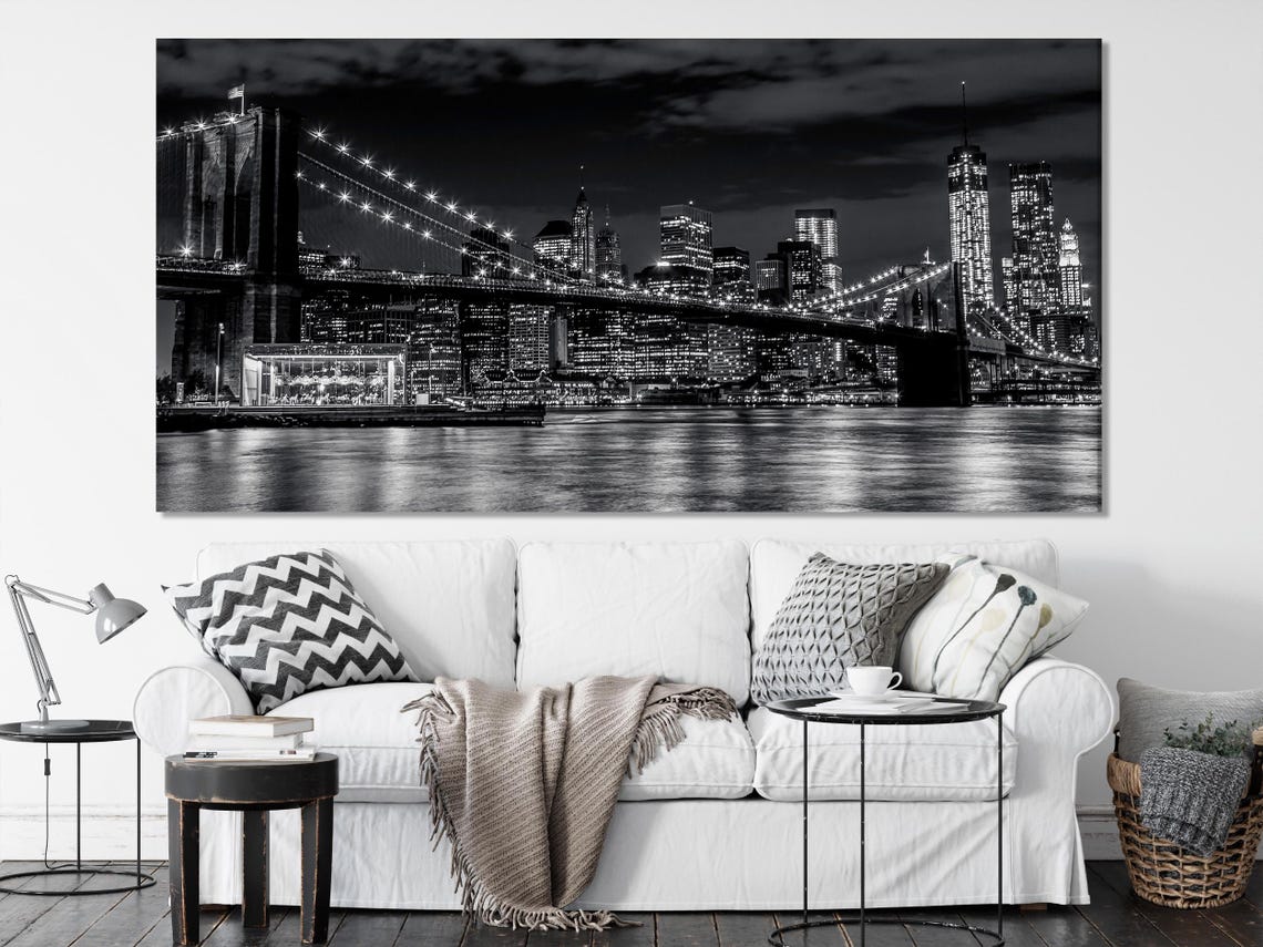 Black-and-white night city skyline with illuminated skyscrapers and a suspension bridge over dark water detail view