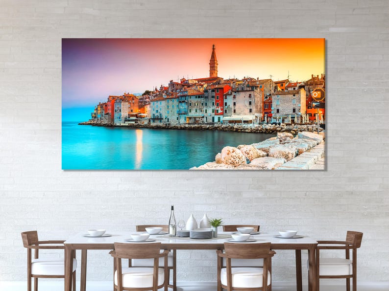 A harbour town at sunset with colourful buildings, a church tower, and turquoise water reflection
