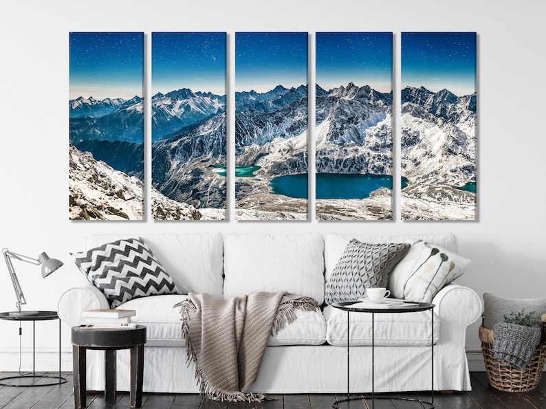 A winter mountain landscape with snow-covered peaks, deep blue starry sky, and turquoise lakes