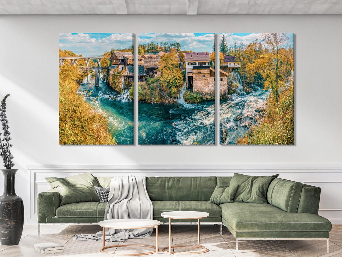 Wide river landscape with turquoise water, waterfalls, autumn trees and a village under a blue sky detail view