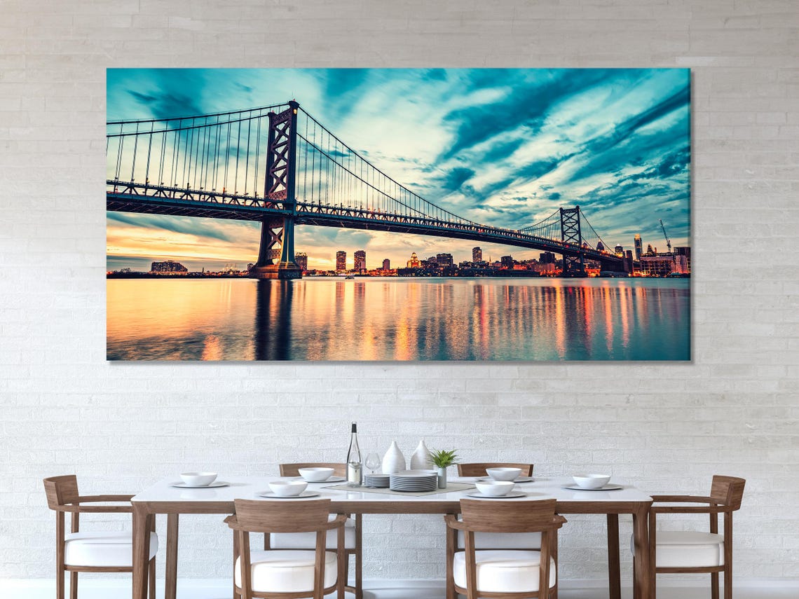 Three-panel suspension bridge cityscape at dusk with teal-blue sky and warm sunset reflections on water detail view