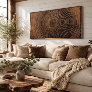 A rectangular wall art piece featuring a detailed dark brown wood grain cross-section with concentric rings, framed in wood. The artwork is displayed above a beige sectional sofa with brown and cream pillows and a chunky knit throw blanket.