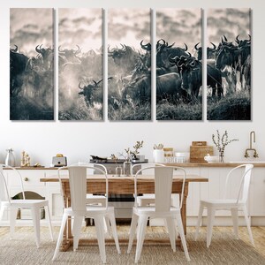 A five-panel canvas print depicting a herd of wildebeest in sepia tones. The animals are tightly packed together, creating a dynamic composition. The background features a hazy sky and indistinct landscape. The overall style is wildlife photography, suitable for home or office decor. The print is ideal for nature and animal lovers.