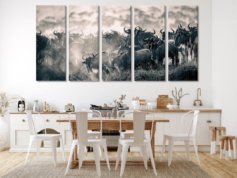 A five-panel canvas print depicting a herd of wildebeest in sepia tones. The animals are tightly packed together, creating a dynamic composition. The background features a hazy sky and indistinct landscape. The overall style is wildlife photography, suitable for home or office decor. The print is ideal for nature and animal lovers.