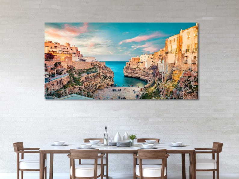 Sunlit cliffside town overlooking a sheltered bay with turquoise blue water and a pastel sky