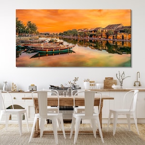 Op de afbeelding: Een kleurrijke zonsondergang boven een rivier in een stad met traditionele gebouwen. Verschillende boten liggen aangemeerd aan de oever.