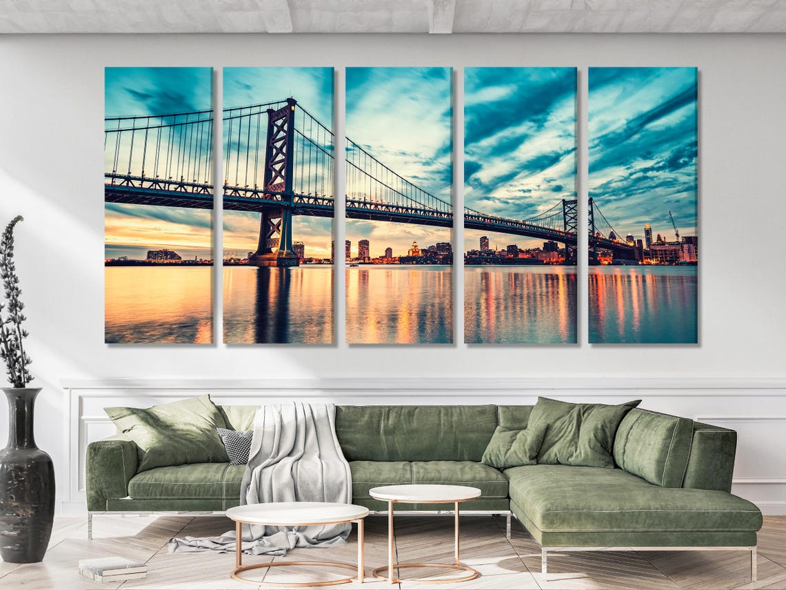 Three-panel suspension bridge cityscape at dusk with teal-blue sky and warm sunset reflections on water detail view
