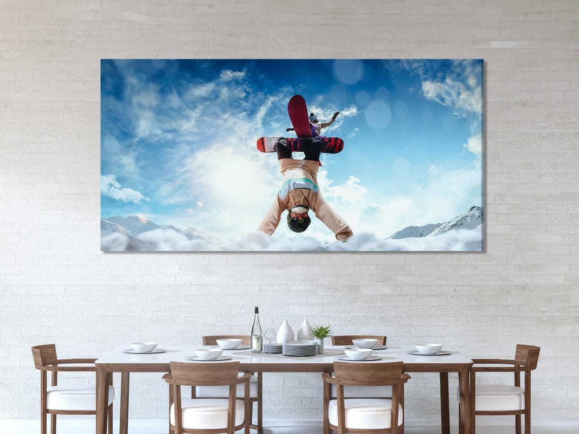 Snowboarder mid-flip against a bright blue sky with snowy mountains in the background detail view