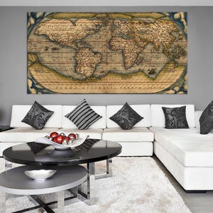 K&ouml;nnte beinhalten: Ein Vintage-Weltkarten-Druck in einem braunen Rahmen h&auml;ngt &uuml;ber einem wei&szlig;en Ecksofa mit schwarz-wei&szlig;en gemusterten Kissen. Ein schwarzer Couchtisch mit einer silbernen Schale mit roten Ornamenten steht vor dem Sofa.