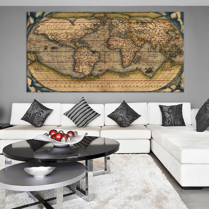 K&ouml;nnte beinhalten: Ein Vintage-Weltkarten-Druck in einem braunen Rahmen h&auml;ngt &uuml;ber einem wei&szlig;en Ecksofa mit schwarz-wei&szlig;en gemusterten Kissen. Ein schwarzer Couchtisch mit einer silbernen Schale mit roten Ornamenten steht vor dem Sofa.