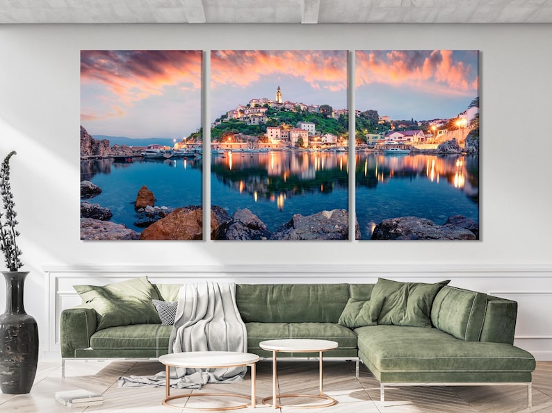 Evening harbour seascape with a hillside town, glowing lights, calm blue water reflections and rocky shore
