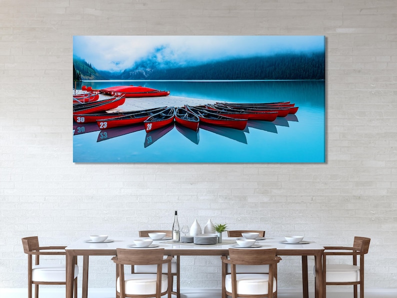 Red canoes docked on calm blue lake water with misty mountains in the background