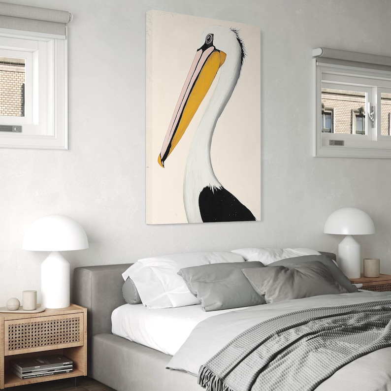 Pu&ograve; includere: Una stampa artistica verticale di un pellicano. L'uccello &egrave; raffigurato di profilo, con un lungo becco giallo e rosa, collo bianco e segni neri. L'opera d'arte &egrave; esposta su una parete sopra un letto in una camera da letto.