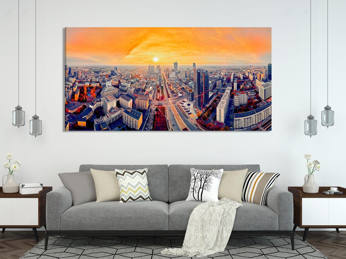 A panoramic city skyline at sunset shows tall buildings and a wide avenue cutting through the streets under a glowing orange sky detail view