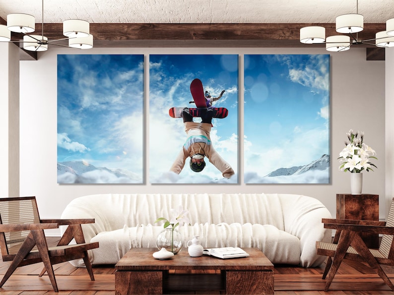 Snowboarder mid-flip against a bright blue sky with snowy mountains in the background