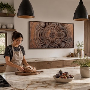 A rectangular wall art piece featuring a detailed, high-contrast wood grain pattern that mimics the concentric rings of a tree trunk cross-section, framed in a dark wood border and mounted horizontally on a plain white wall.