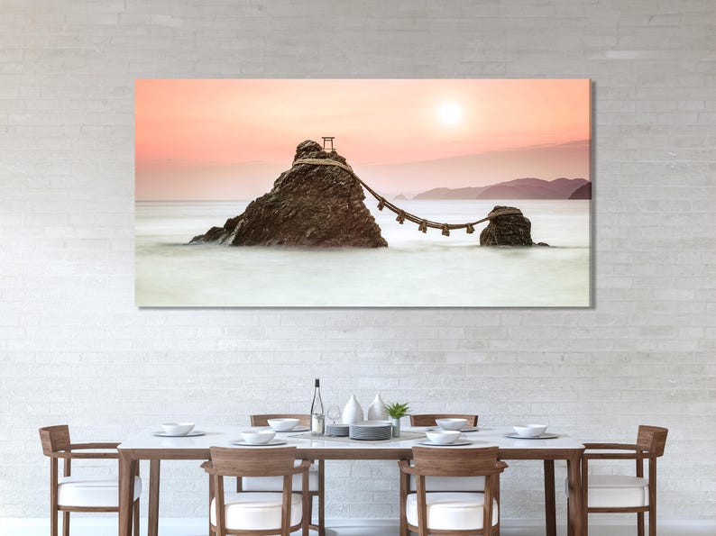 A sunset seascape shows two rocky islands connected by a rope with small posts, set against soft pink-orange skies and pale misty water