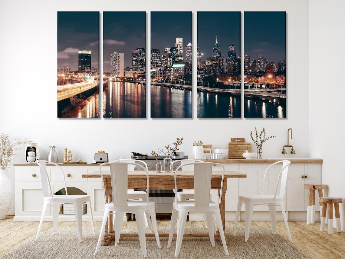 A night city skyline stretches across a wide river, with glowing building lights and shimmering reflections under a deep blue sky detail view