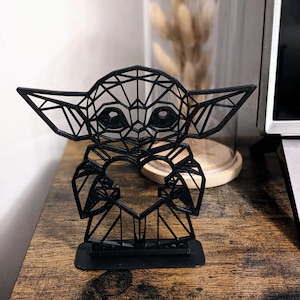 Peut inclure: Une sculpture géométrique 3D noire d'un personnage fictif populaire tenant un cœur. La sculpture est faite de métal noir fin et repose sur une base noire.