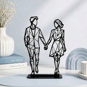 Peut inclure: Une sculpture en métal noir représentant la silhouette géométrique et filaire de deux personnages se tenant la main. Les figures reposent sur une base rectangulaire, formées par des lignes angulaires nettes créant un aspect moderne et abstrait.