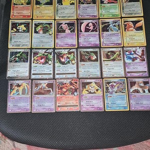 Puede incluir: Una colección de veinticuatro cartas coleccionables rectangulares dispuestas en cuatro filas de seis. Cada carta presenta una ilustración colorida única de una criatura, junto con texto impreso que detalla nombres, estadísticas y habilidades de juego.