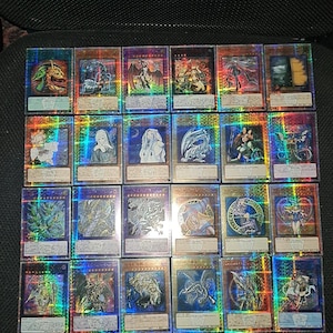 May include: A selection of holographic trading cards, depicting fantasy creatures and characters. The cards have a shimmering, rainbow effect and are arranged on a dark surface.