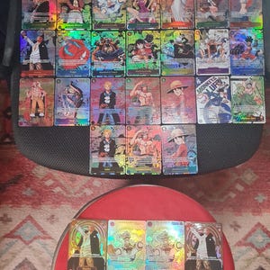 Puede incluir: Colección de cartas coleccionables holográficas con ilustraciones de personajes coloridos. Las cartas tienen una superficie brillante y reflectante. Están dispuestas sobre una superficie oscura y una mesa roja.