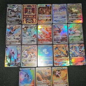 May include: A collection of colorful trading cards featuring various characters and designs. The cards have holographic and foil accents, with different HP values and character names visible. The cards are arranged on a dark surface.