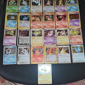 Può includere: Una collezione di venticinque carte collezionabili Pokémon rettangolari disposte a griglia. Ogni carta presenta un'illustrazione colorata unica di una creatura, testo in giapponese e varie statistiche di gioco su uno sfondo bianco e colorato.