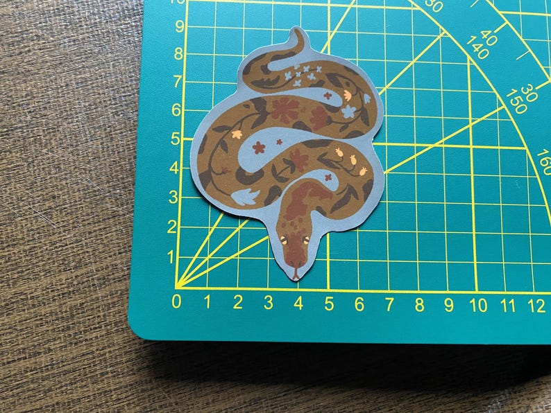 May include: A brown and blue snake sticker with floral designs. The snake is curled up in a circle with its tail in its mouth.
