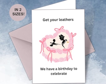 May include: A white birthday card with the text "Get your leathers" and "We have a birthday to celebrate". The card features a pink cake design with two black dragons. A pink envelope is visible.