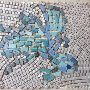 May include: A close-up of a mosaic art piece with a design of blue and gray tiles. The tiles are arranged in a pattern that resembles a flower or a star.