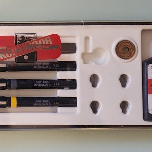 May include: A set of Koh-I-Noor Rapidograph SL drawing pens and ink in a plastic case. The set includes black pens, ink, and accessories. The ink bottle is labeled "3080-F Black Waterproof India Drawing Ink".