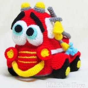 May include: A red, yellow, and black crocheted fire truck toy with big, googly eyes. The truck has a hose and a ladder.