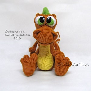 May include: A crocheted orange and yellow dragon toy with green horns and large white eyes. The dragon is sitting with its legs crossed and has a small white wing on its back. The text "@LilikSha Toys crochettoy.jimdo.com 2018" is visible on the image.
