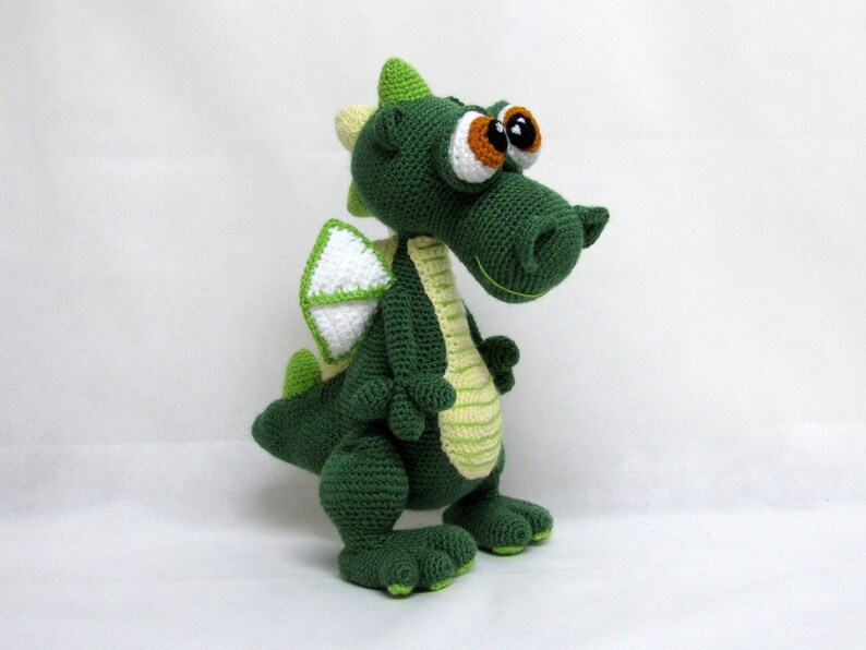 May include: Green crocheted dragon toy with large eyes and a white wing. The dragon has a light green stripe down its back.