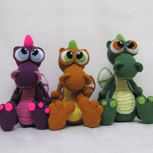 May include: Three crocheted plush dragons, one purple, one orange, and one green, with large eyes and a whimsical expression.