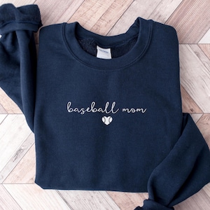 May include: Navy blue sweatshirt featuring the text "baseball mom" in a cursive script, with a baseball graphic beneath. The garment is made of a soft fabric, suitable for everyday wear.